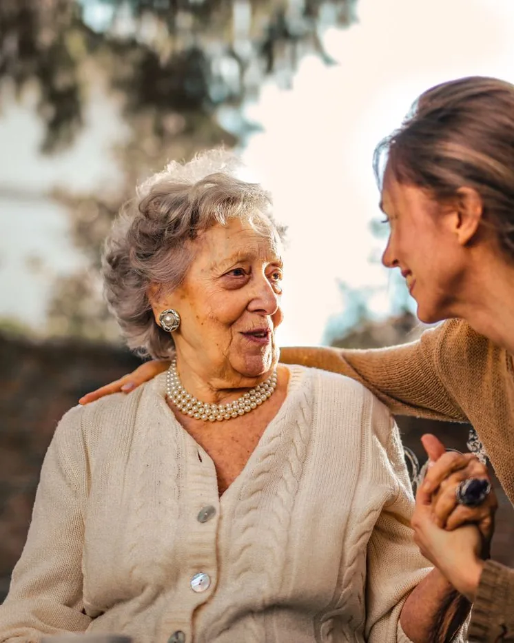 Une femme âgée et une femme plus jeune se tiennent la main, en extérieur.