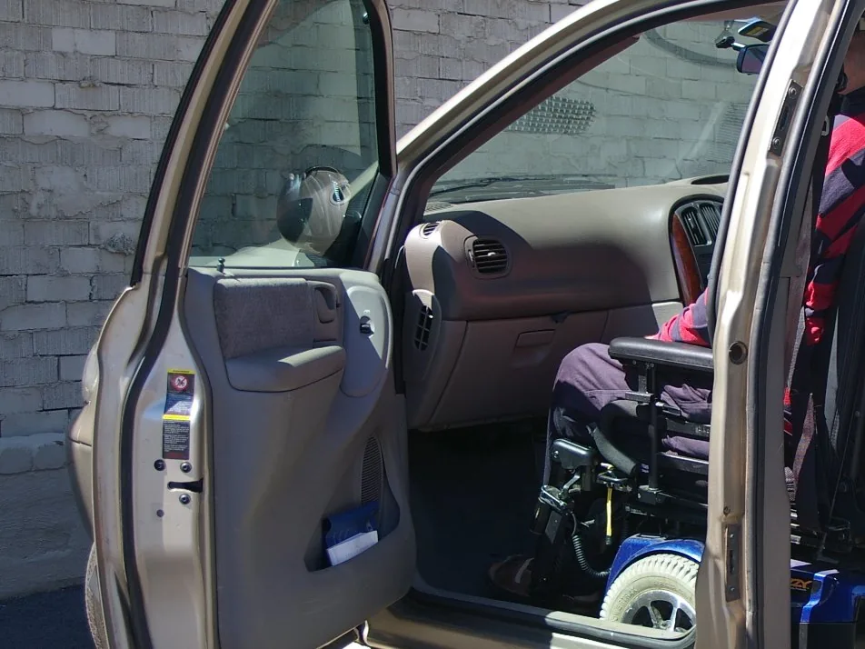 Personne en fauteuil roulant installée à l’intérieur d’un véhicule adapté.